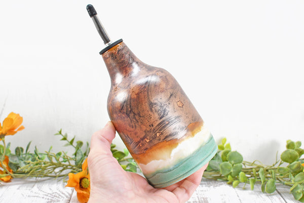 Hand holding Copper, Green, and White glazed Ceramic Olive Oil Dispenser. Handmade Pottery Liquid Soap Bottle for Bathroom and Kitchen Decor. Camille Woodward artist.