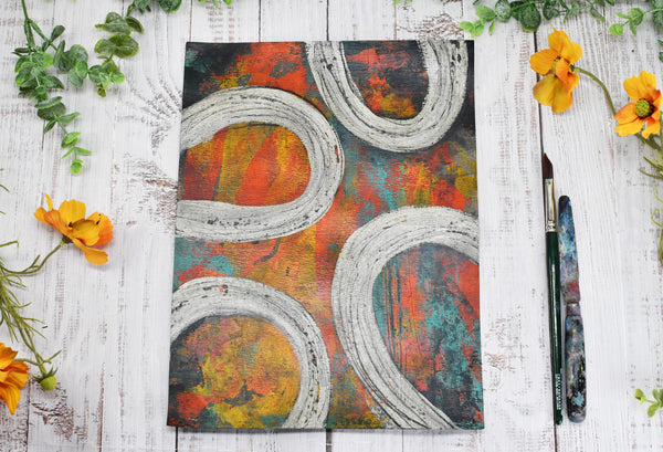 Abstract Painting, Original Mixed Media Orange and Gray Wall Art painting on Paper with a paintbrush and palette knife beside it, on a table. Hand painted by artist Camille Woodward.